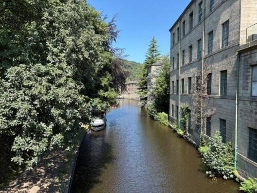 The Rochdale Canal running between trees and old mill buildings in Hebden Bridge