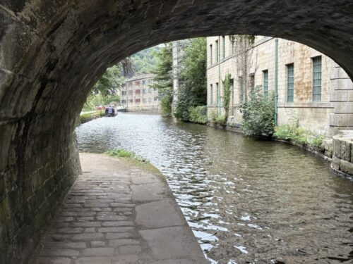 View from under the canal bridge along the Rochdale Canal towards old mill buildings in Hebden Bridge